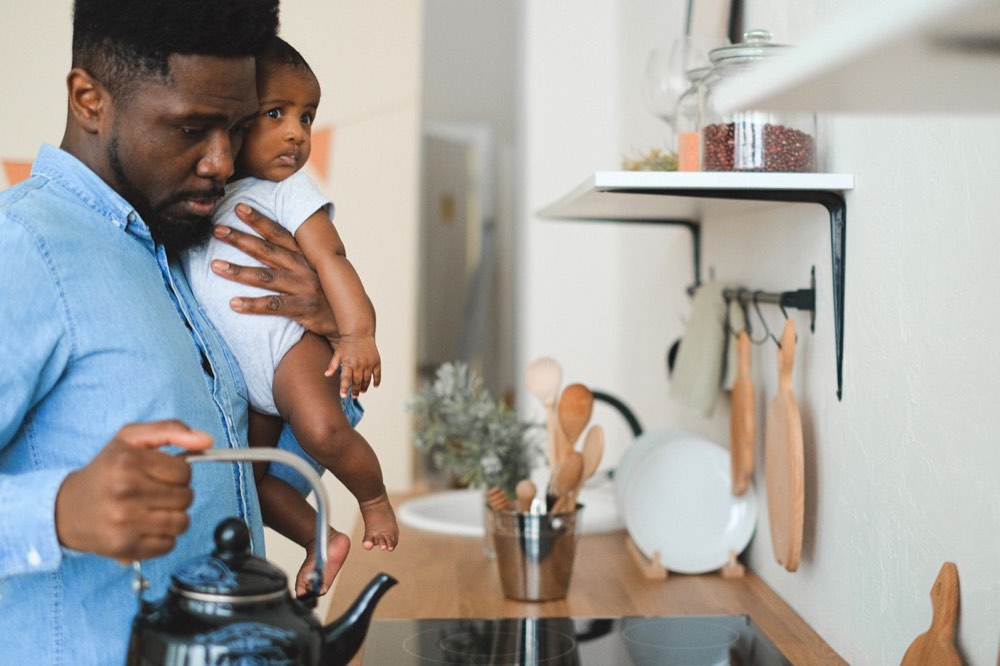A parent holds a baby in a sunlit kitchen